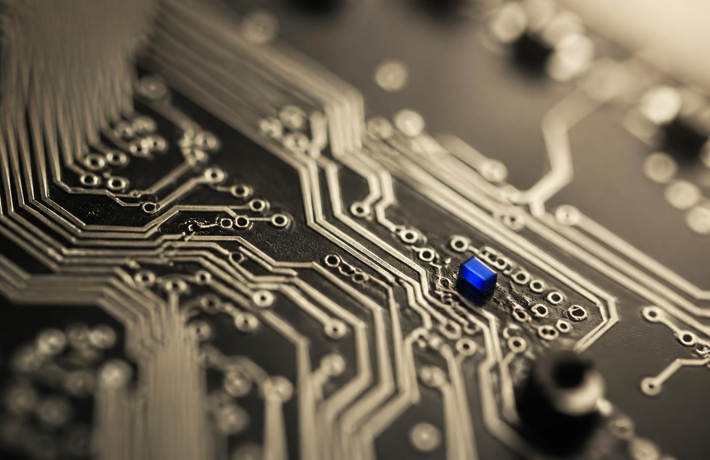 Macro photograph of a circuit board showing fine traces and one blue component